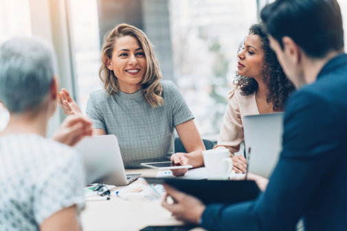 Stock image of staff members in an office consulting around a table.